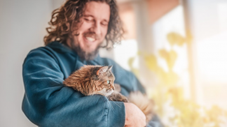 bearded-man-hugging-cat-by-window-with-flowerpots-sunlight-scaled